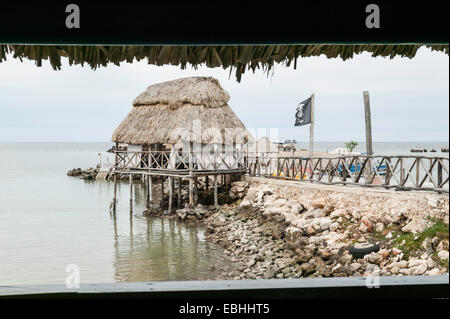 Toit de chaume patio salle à manger surélevée au-dessus de l'eau avec drapeau pirate en lambeaux dans le vent, dans la baie de Campeche, Campeche, Mexique. Banque D'Images