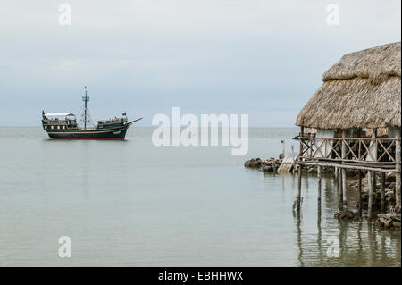 Approche d'un bateau de pirates avec dock artificiel et toit de chaume patio salle à manger au-dessus de l'eau, de la baie de Campeche, Campeche, Mexique. Banque D'Images