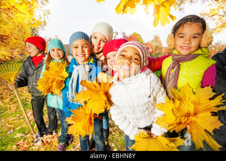 Groupe d'enfants avec le râteau et bouquets de feuilles jaunes Banque D'Images