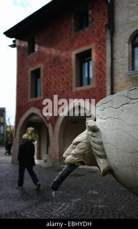 Fontaine avec tête de lion en face d'un édifice gothique avec sa façade est décorée de fresques complet. Vieille ville de Pordenone. L'Italie. Banque D'Images