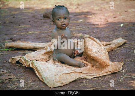 Jeune enfant de sexe féminin dans une région pauvre, assis sur un sac en plastique avec un ventre qui est gonflé par les vers et de la malnutrition, de l'Ouganda, Jinja Banque D'Images