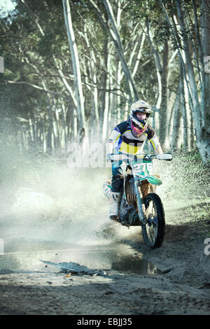 Jeune homme motocross racer équitation à travers la forêt en flaque Banque D'Images