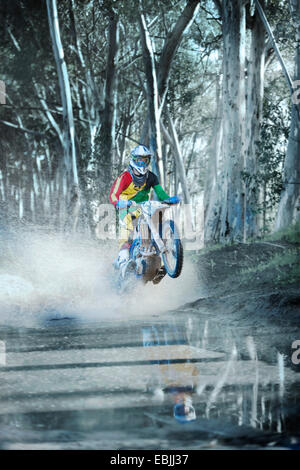 Jeune homme motocross racer équitation à travers un chemin de terre flaque en forêt Banque D'Images