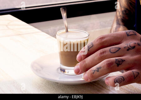 La main tatouée de jeune homme et du café shotglass sur cafe table Banque D'Images