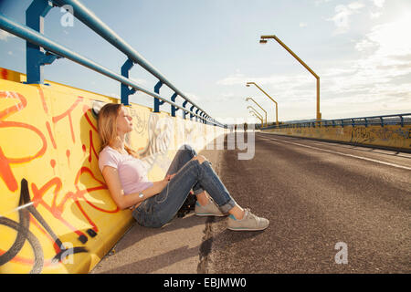 Young woman leaning against wall graffiti sur le pont en plein soleil Banque D'Images
