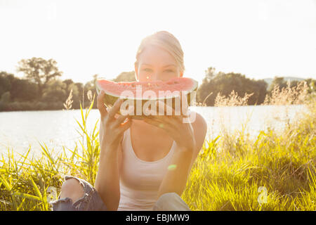 Portrait of young woman holding up tranche de melon en face de face, l'île du Danube, Vienne, Autriche Banque D'Images