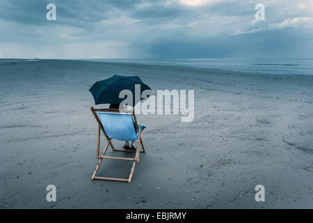 Couple assis sur une chaise longue sur la plage, sous égide orageux Banque D'Images