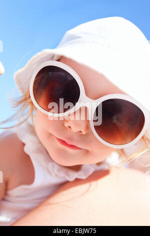 Petite fille avec des lunettes de soleil sur les bras des mères smiling à l'appareil photo Banque D'Images