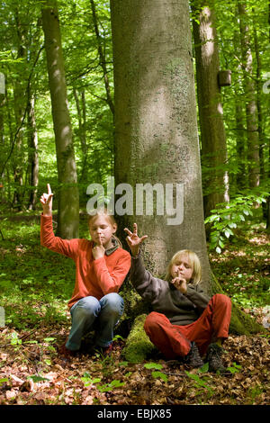 Deux enfants assis avec les yeux fermés dans une forêt au printemps, à l'écoute de chants, en comptant les différentes espèces, Allemagne Banque D'Images