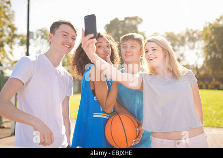 Quatre jeunes joueurs de basket-ball adultes prenant selfies smartphone Banque D'Images