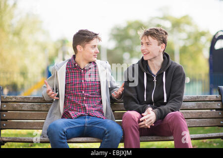 Deux jeunes hommes friends chatting on park bench Banque D'Images