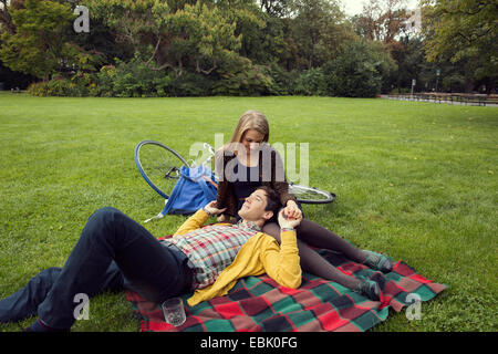 Young couple holding hands on picnic blanket in park Banque D'Images