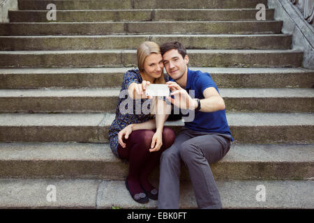 Jeune couple assis sur l'escalier vieille rue posant pour selfies smartphone Banque D'Images