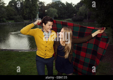 Young couple holding up blanket in park Banque D'Images