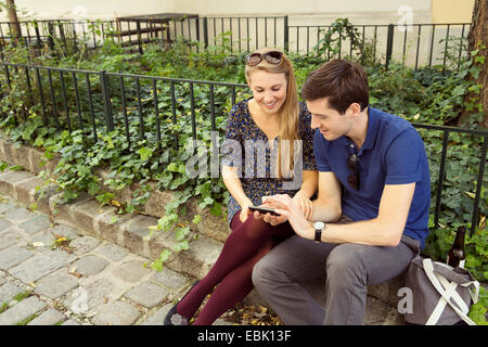 Young couple sitting on wall looking down at smartphone Banque D'Images