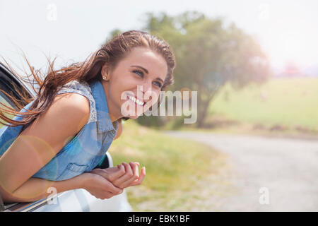 Young woman leaning out of car window on road trip Banque D'Images