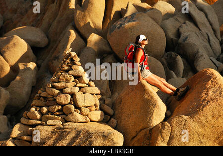 Wanderer femme assis sur une pierre à côté pile de pierres et de profiter du soleil, France, Corse, Capu di Muru Banque D'Images