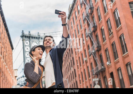 USA, l'État de New York, New York City, Brooklyn, couple qui, dans la rue selfies Brooklyn Bridge en arrière-plan Banque D'Images