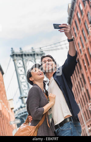 USA, l'État de New York, New York City, Brooklyn, couple qui, dans la rue selfies Brooklyn Bridge en arrière-plan Banque D'Images