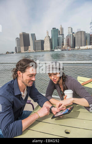 USA, l'État de New York, New York City, Brooklyn, heureux couple assis et à l'aide de tablet pc avec cityscape in background Banque D'Images