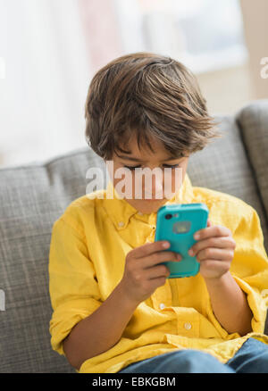Boy (6-7) sitting on sofa and using cell phone Banque D'Images
