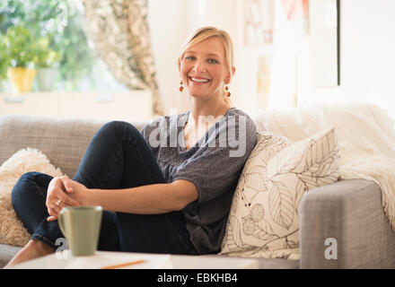 Woman sitting on sofa in living room Banque D'Images