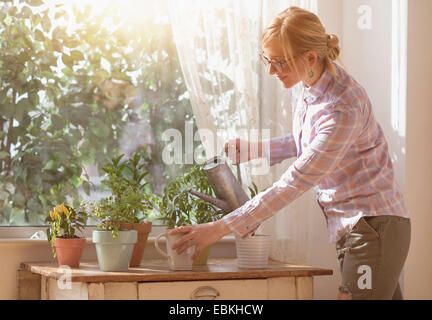 Woman watering plants in living room Banque D'Images