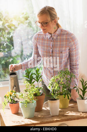 Woman watering plants in living room Banque D'Images