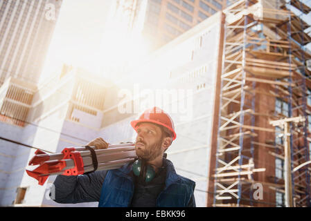 Construction Worker carrying trépied sur l'épaule Banque D'Images