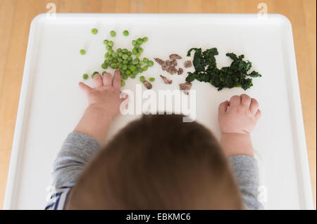 Baby Girl (12-17 mois) de manger des steaks, les épinards et les pois verts Banque D'Images