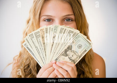 Girl (12-13) holding fan d'argent contre son visage Banque D'Images