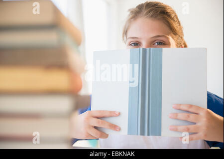 Teenage girl (12-13) se cacher derrière face book Banque D'Images