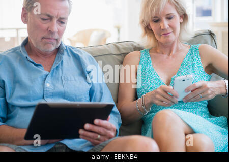 Portrait of couple sitting on sofa using digital tablet et smart phone Banque D'Images