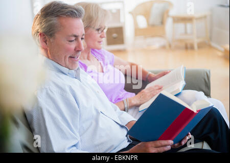 Portrait of couple sitting on sofa reading books Banque D'Images