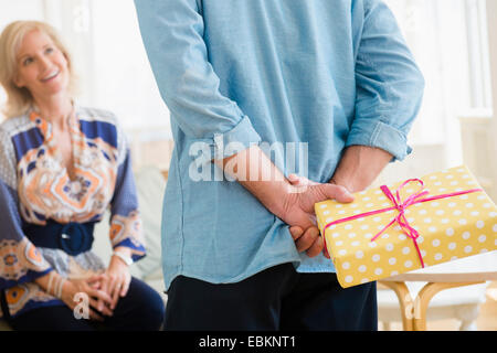 Vue arrière du man holding wrapped anniversaire présents derrière retour debout devant smiling woman Banque D'Images