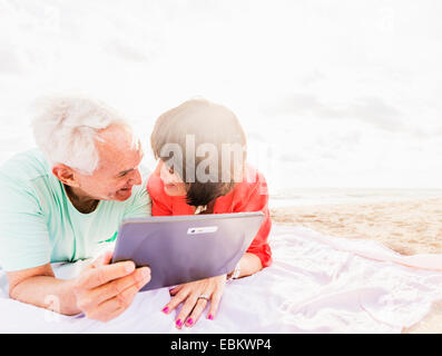 USA, Floride, Jupiter, Couple with digital tablet lying on blanket at beach Banque D'Images