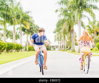 USA, Floride, Jupiter, jeune couple roulant vélos le long de rue avec palmiers Banque D'Images