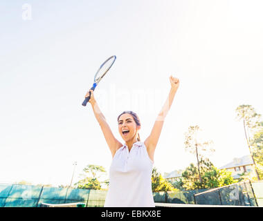 USA, Floride, Jupiter, Portrait of young woman holding tennis racket, raising arms à celebration Banque D'Images