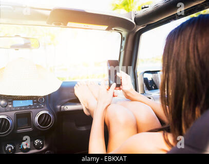 USA, Floride, Jupiter, young woman sitting in car avec les jambes sur le tableau de bord à l'aide de smart phone Banque D'Images