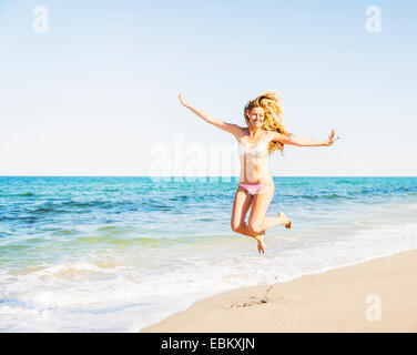USA, Floride, Jupiter, Portrait of young woman wearing bikini jumping on beach Banque D'Images