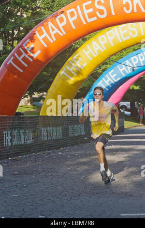 Homme runner courir vite éclaboussé de teintures colorées s'approche de la ligne d'arrivée dans l'heureux l'Asheville 5K Color Run Banque D'Images