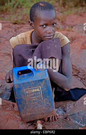 Fille est assis au bord de la rivière nil avec un vieux bidon d'huile lourde qu'elle utilise pour aller chercher de l'eau, de l'Ouganda, Jinja Banque D'Images