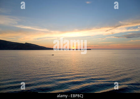 Ia, Santorin, Grèce, sud de la Mer Egée. Vue sur mer à l'île de Thirasia et le coucher du soleil, petit bateau qui passe. Banque D'Images