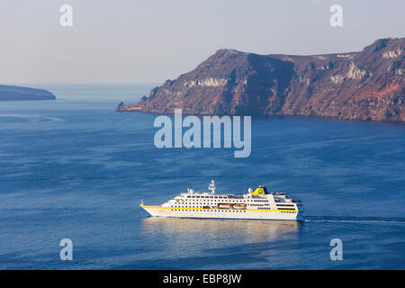 Ia, Santorin, Grèce, sud de la Mer Egée. Bateau de croisière traversant la caldeira sous les falaises d'un rouge profond de l'île de Thirasia. Banque D'Images