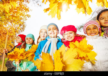 Beaucoup d'enfants souriants avec le râteau et feuilles jaunes Banque D'Images