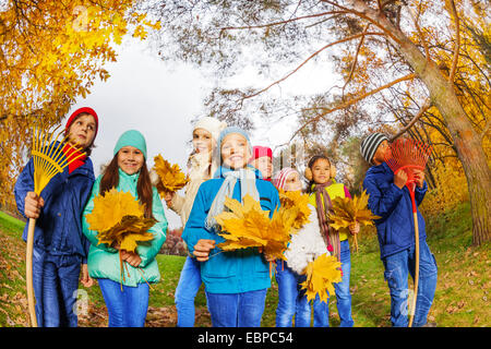 Rangée d'enfants heureux avec les râteaux et les bouquets de feuilles Banque D'Images