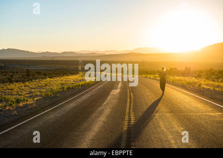 Femme marchant sur une longue route sinueuse au coucher du soleil dans l'est du Nevada, États-Unis d'Amérique, Amérique du Nord Banque D'Images