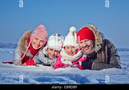 Couple heureux et deux enfants en winterwear couché dans la neige Banque D'Images