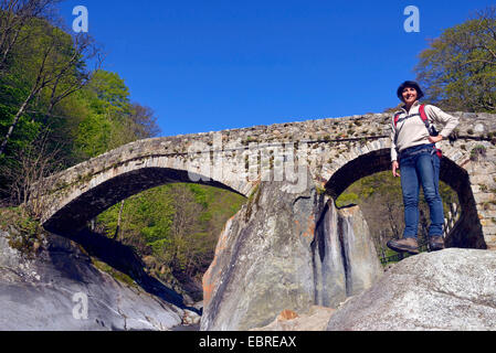 Wanderer femelle à Rocky River lit en face d'un pont de pierre, Italie, Piémont, Biella, Piedicavallo Banque D'Images