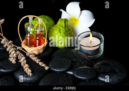 Concept spa aromatique de bouteilles huile essentielle de bergamote, fruits, plumeria flower, bougie et lavandes séchées sur le zen stones Banque D'Images